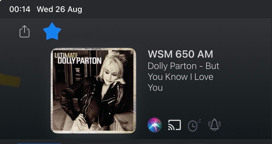 Screen clip from the MyTuner App showing the WSM 650 AM radio station, current song playing: Dolly Parton – But You Know I Love You. The album cover showing is Ultimate Dolly Parton, where she is wearing a black leather jacket and leaning on her elbow against a counter… contemplating…