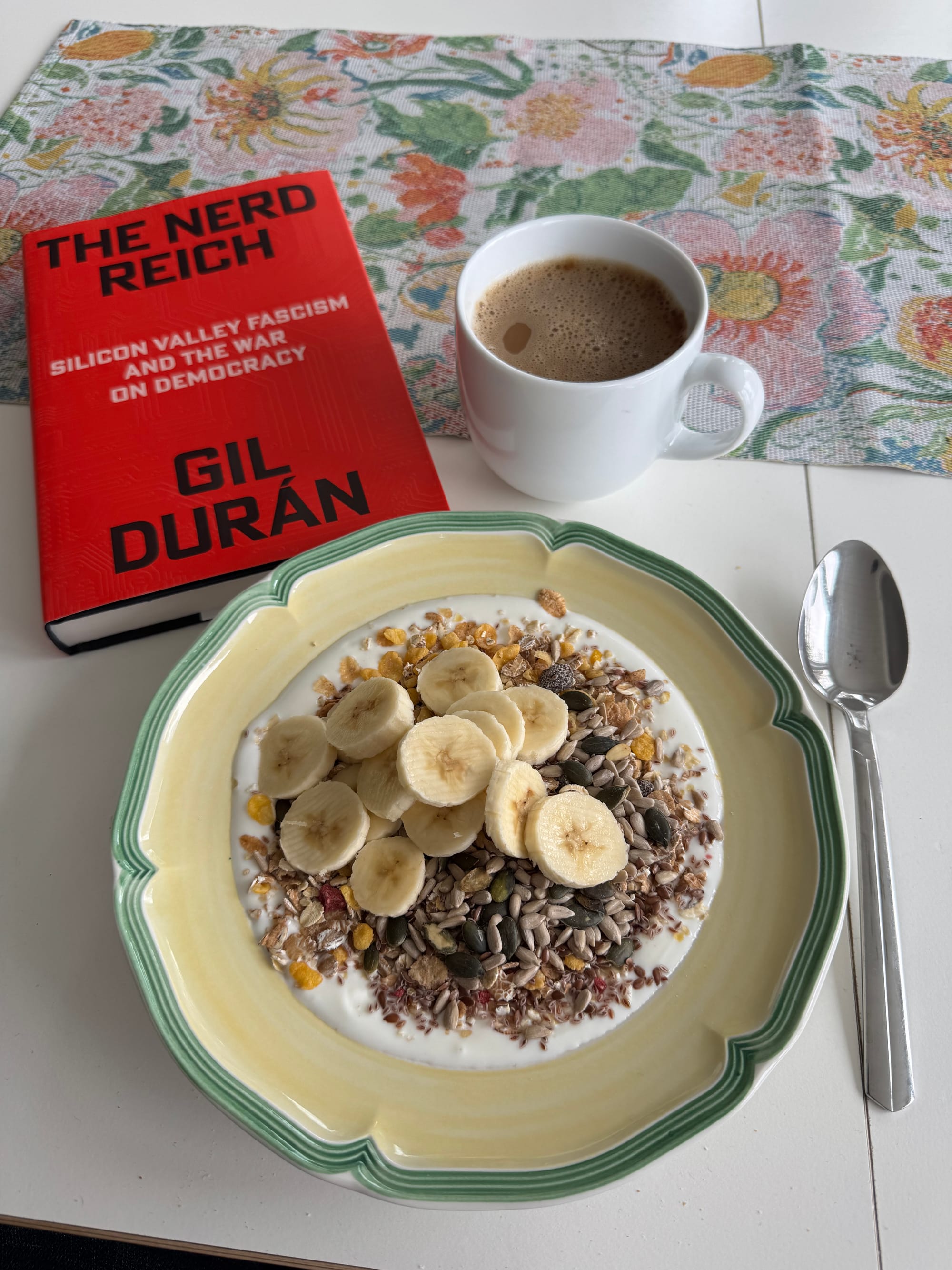 Boken 'The Nerd Reich' av Gil Durán på ett bord tillsammans med en tallrik filmjölk med müsli och skivad banan, och en stor mugg kaffe. Bokens undertitel är 'Silicon Valley fascism and the war on democracy'.