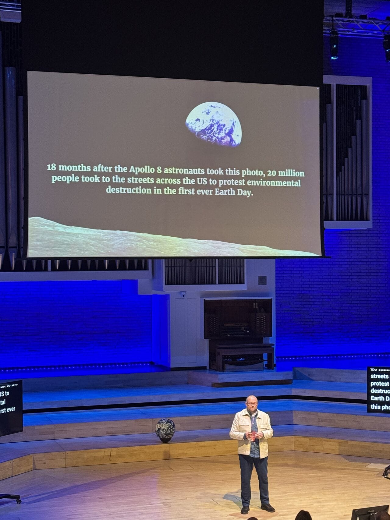 Per Axbom on stage. Photo of an 'earthrise' by William Anders in 1968. Text on slide: "18 months afther the Apollo 8 astronatus took this photo, 20 million people took to the streets across the US to protect environmental destruction in the first ever Earth Day."